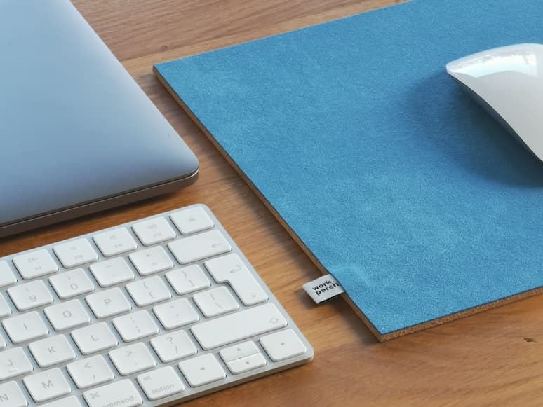 A close-up of a blue desk mat beside a keyboard, laptop, and mouse on a wooden desk.