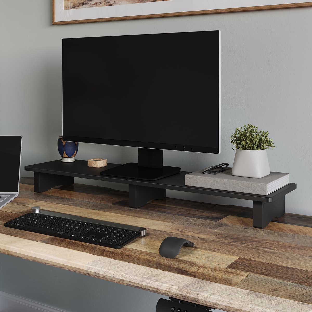 A black desk shelf holding a monitor above a keyboard and accessories on a standing desk.