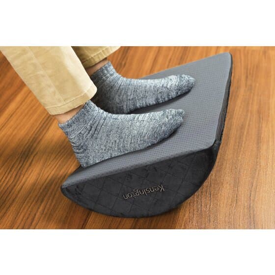 A black cushioned office footrest with a gray adjustable base viewed at an angle.