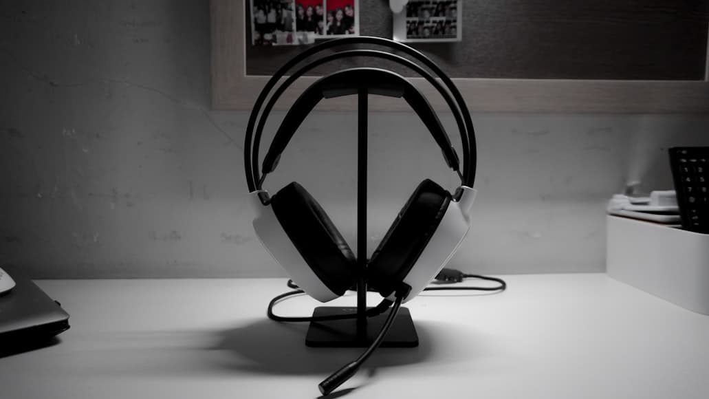 A white over-ear gaming headset resting on a black stand on a white desk.