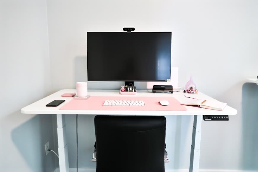 A small white desk with a single monitor, keyboard, mouse, and notebook arranged in a clean centered layout.