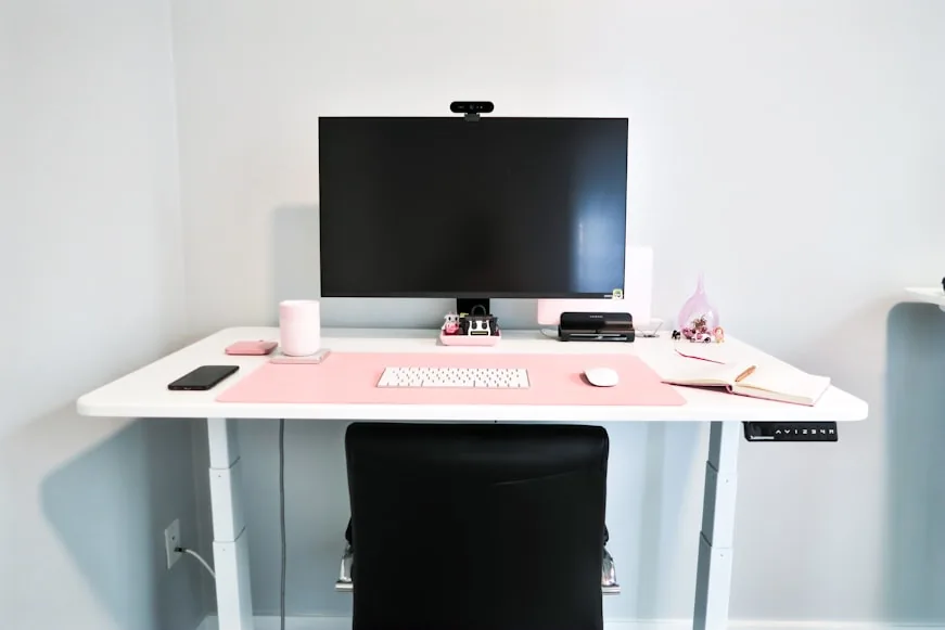 A small white desk with a single monitor, keyboard, mouse, and notebook arranged in a clean centered layout.