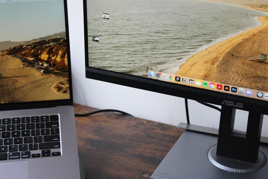 An open laptop beside an external monitor in a compact desk setup.