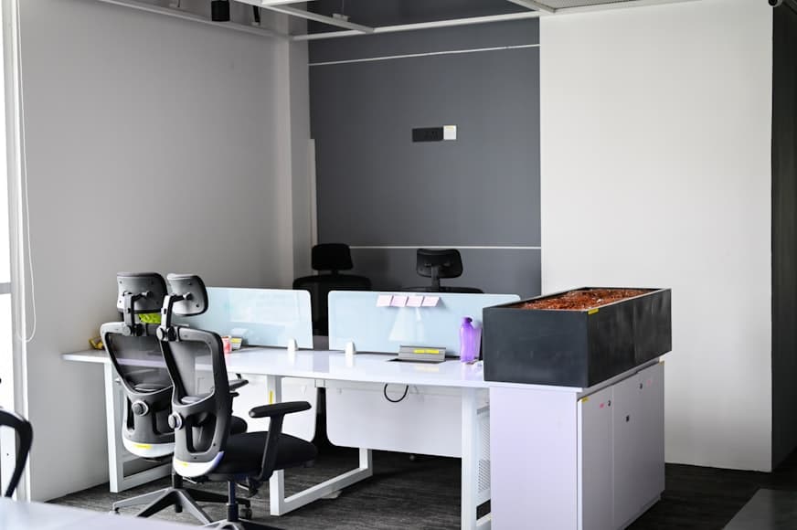 Two black office chairs at white desks in a bright minimalist workspace.