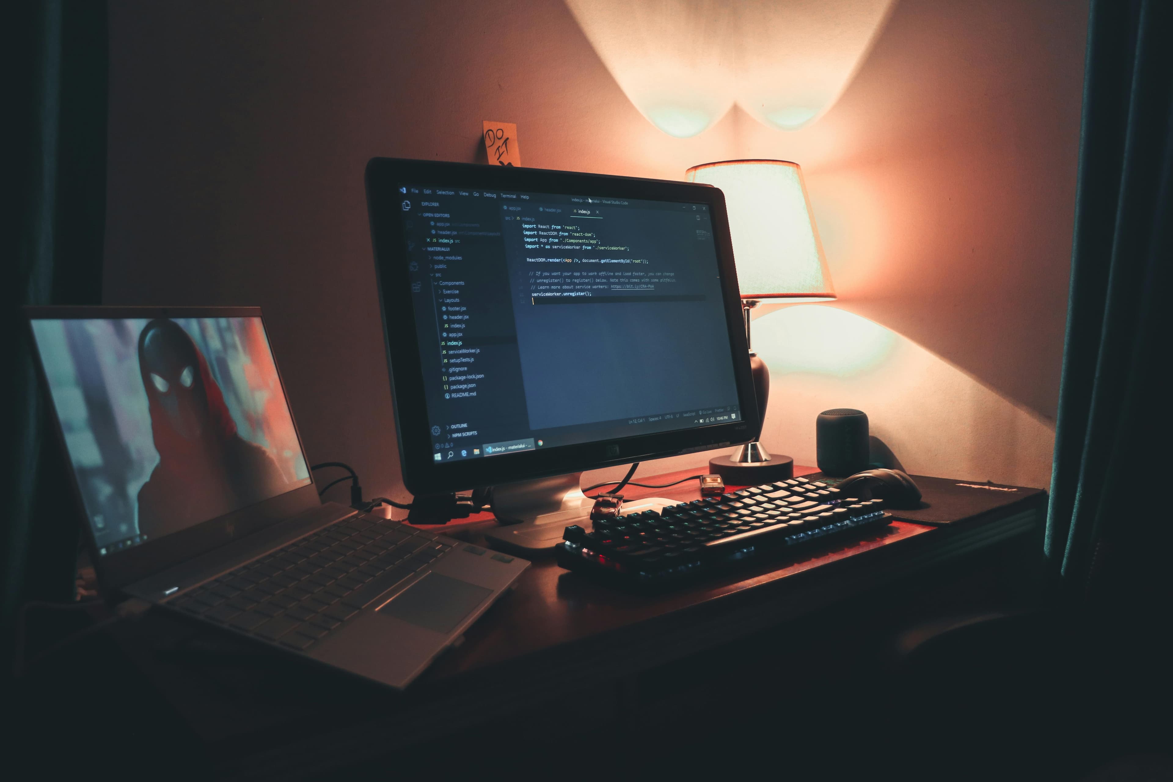 A person at a desk writing in a notebook beside a laptop and workspace items.