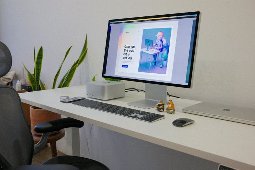 A tidy desk setup with a monitor, laptop, keyboard, and chair in a bright room.