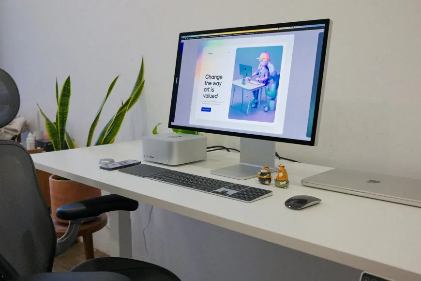 A tidy desk setup with a monitor, laptop, keyboard, and chair in a bright room.