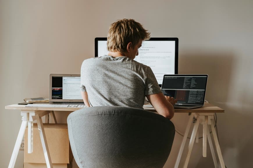 A seated work setup with a desk, chair, and laptop in a bright room.