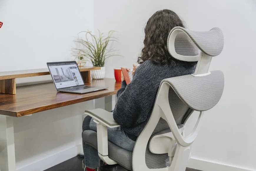 A clean desk setup with an ergonomic chair, monitor, and plants in a bright room.