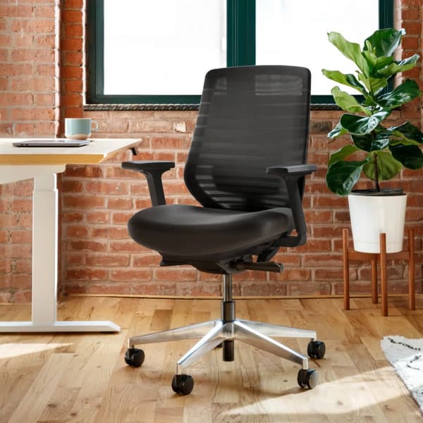 Branch Ergonomic Chair shown beside a compact desk in an official lifestyle image.