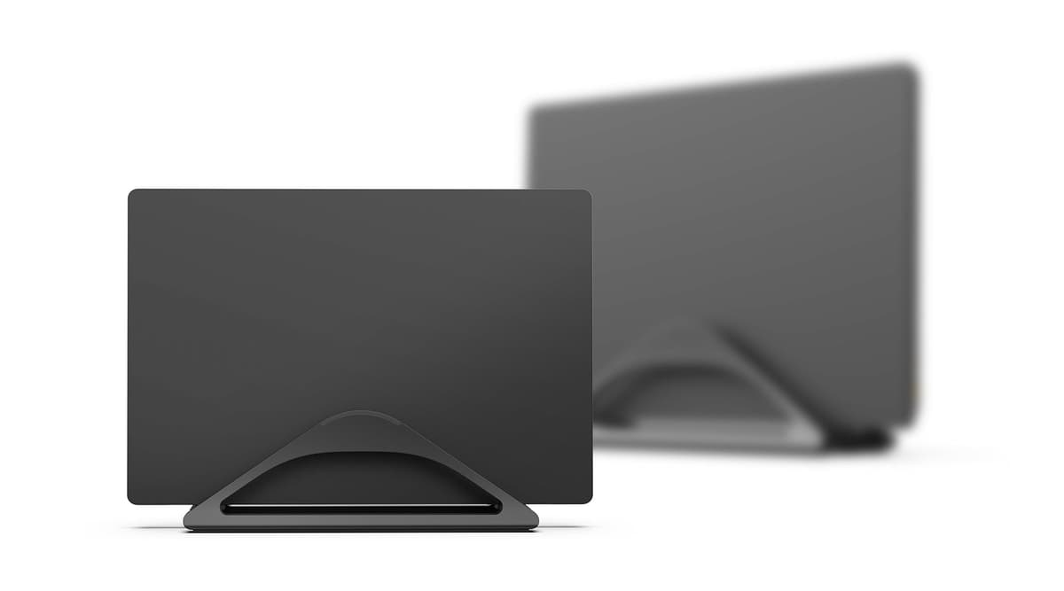 A closed laptop docked vertically in a HumanCentric stand beside an external monitor and keyboard.