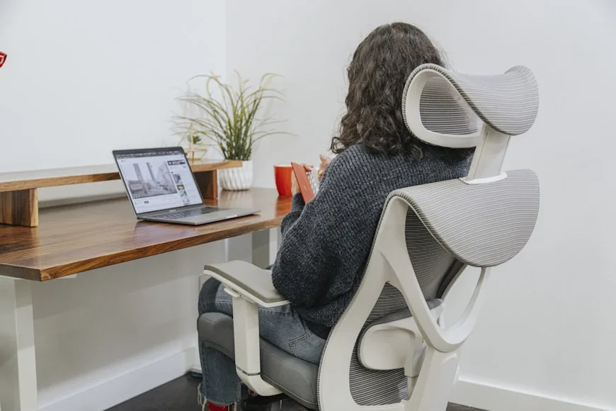 A clean desk setup with an ergonomic chair, monitor, and plants in a bright room.