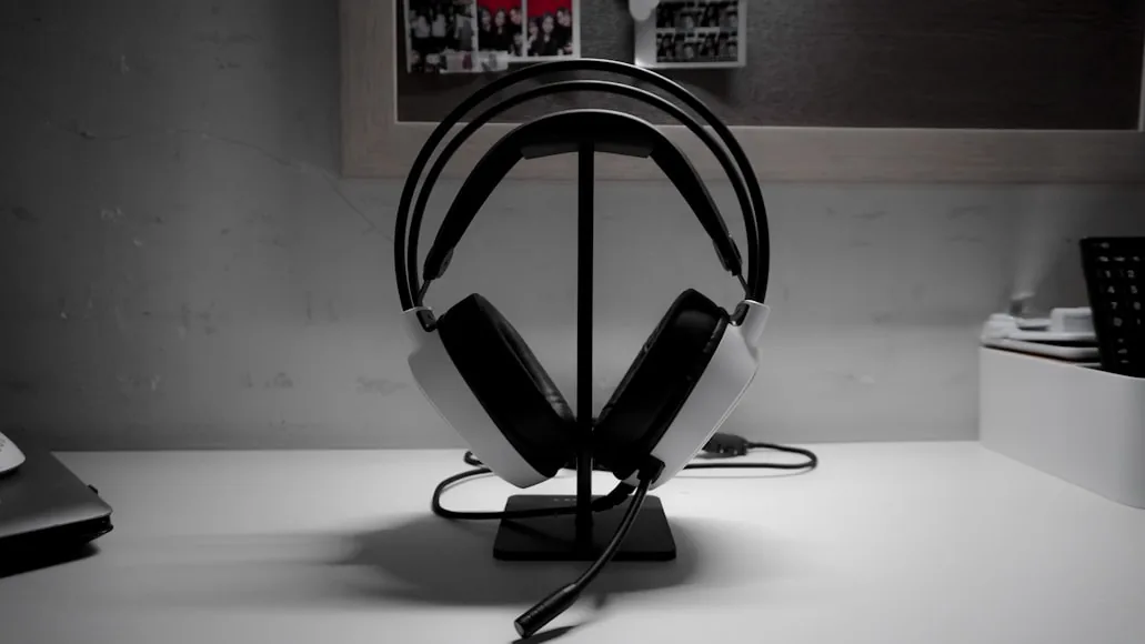 A white over-ear gaming headset resting on a black stand on a white desk.