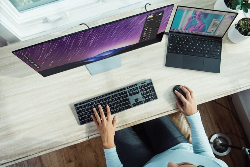 A modern desk setup with an external monitor, an open laptop, and a keyboard arranged for side-by-side work.