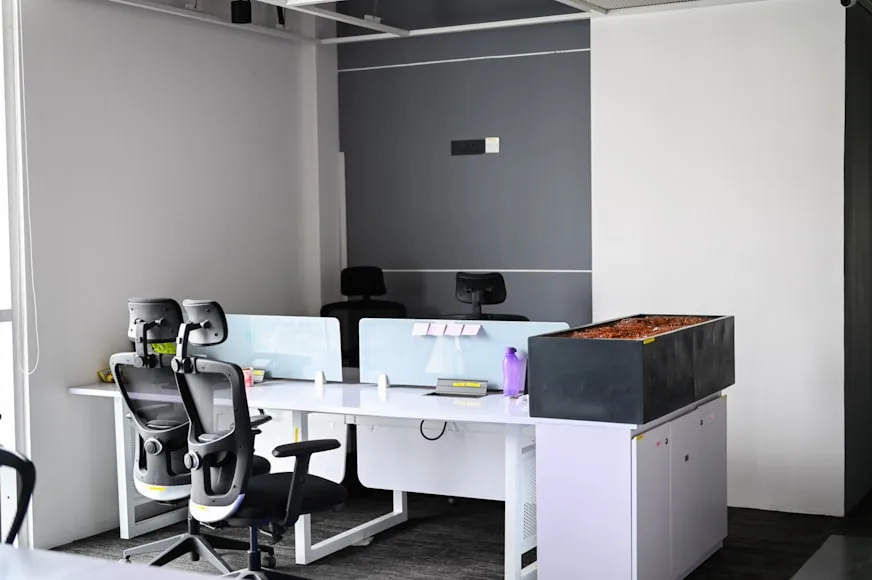 Two black office chairs at white desks in a bright minimalist workspace.