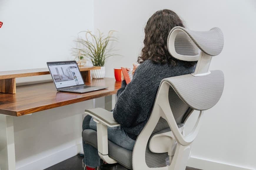 A clean desk setup with an ergonomic chair, monitor, and plants in a bright room.