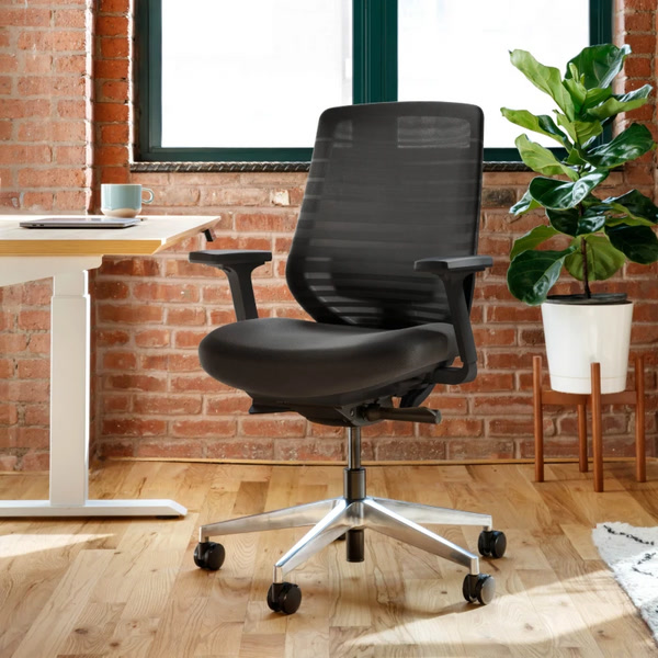 Branch Ergonomic Chair shown beside a compact desk in an official lifestyle image.